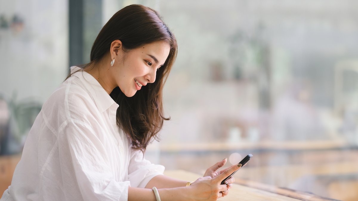 Khách hàng mỉm cười đọc tin nhắn trên điện thoại, minh họa tin nhắn chúc mừng sinh nhật khách hàng